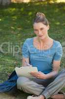 Relaxed young woman writing on clipboard at park