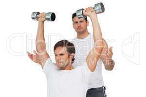 Male trainer assisting man with dumbbells