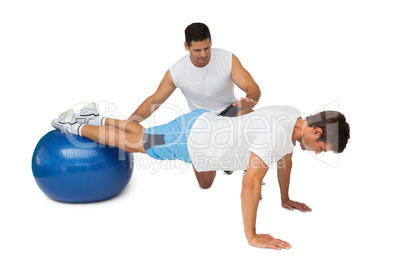 Trainer helping young man exercise on fitness ball