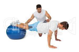Trainer helping young man exercise on fitness ball