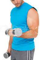 Mid section of a fit man exercising with dumbbells