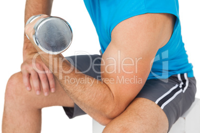 Mid section of a fit man exercising with dumbbell