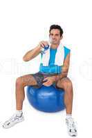 Fit man sitting on exercise ball while drinking water