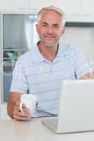 Casual smiling man using his laptop while having coffee
