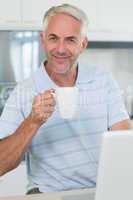 Smiling man using his laptop while having coffee