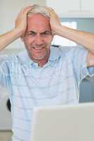 Stressed man using his laptop looking at camera