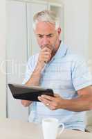 Thoughtful man using his tablet at breakfast