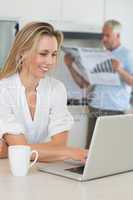 Smiling woman using laptop with partner standing with the paper