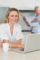 Happy woman using laptop with partner standing with the paper