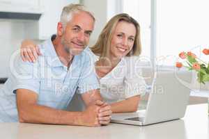 Cheerful couple using laptop together smiling at camera