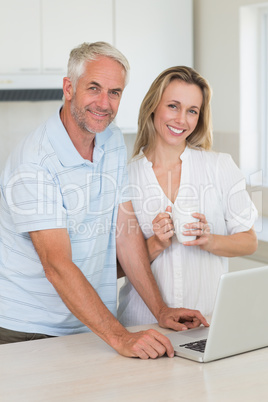 Cheerful couple using laptop together having coffee smiling at c