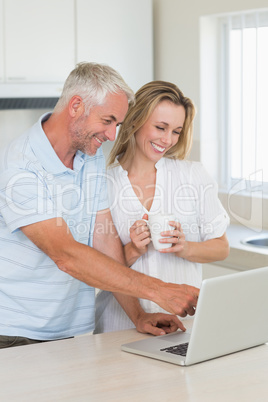 Cheerful couple using laptop together having coffee