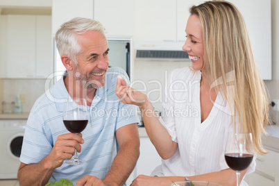 Cheerful couple preparing dinner together and drinking red wine