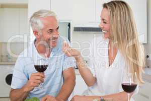 Cheerful couple preparing dinner together and drinking red wine