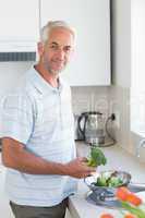 Casual man rinsing broccoli in colander and smiling at camera