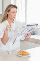 Serious woman holding mug and newspaper at breakfast