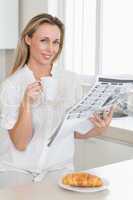 Happy woman holding mug and newspaper at breakfast