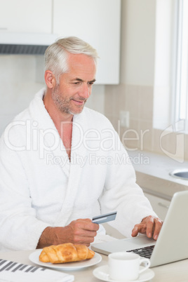 Happy man shopping online at breakfast in a bathrobe