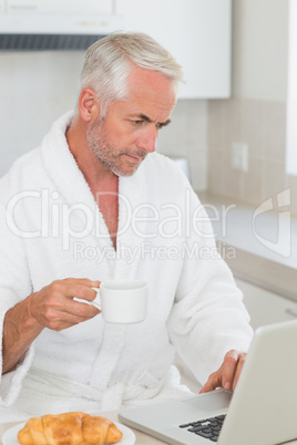 Serious man using laptop at breakfast in a bathrobe