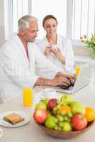Smiling couple using laptop at breakfast in bathrobes