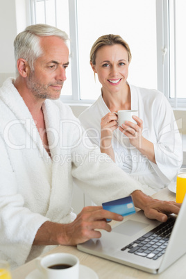 Smiling couple using laptop at breakfast in bathrobes