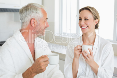 Smiling couple having coffee at breakfast in bathrobes