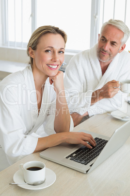 Couple having coffee at breakfast in bathrobes using laptop