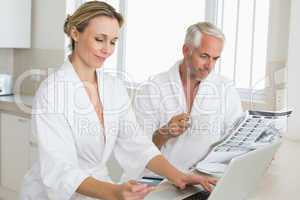 Couple shopping online and reading newspaper in bathrobes