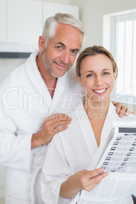 Happy couple reading newspaper together in bathrobes