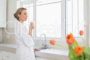 Thoughtful woman in bathrobe standing with coffee cup