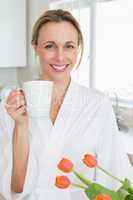 Smiling woman in bathrobe standing with coffee cup