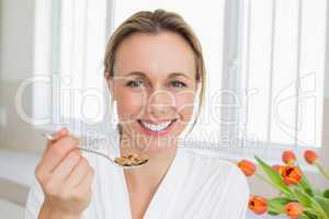 Smiling woman in bathrobe having cereal