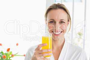 Smiling woman in bathrobe having glass of orange juice