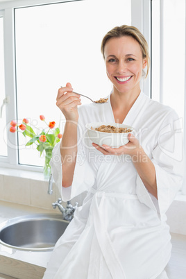 Smiling woman in bathrobe having cereal