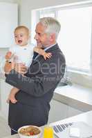Smiling businessman holding his baby in the morning before work
