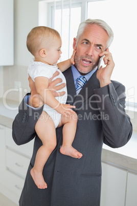 Distracted businessman holding his baby in the morning before wo