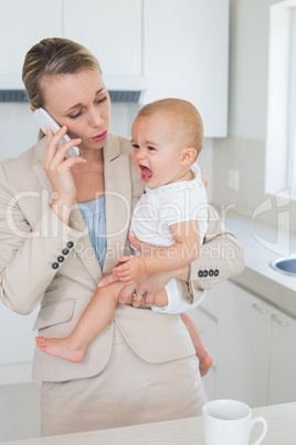 Businesswoman holding her crying baby talking on the phone