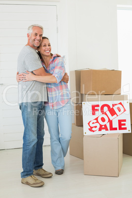 Happy couple standing and hugging beside sold sign