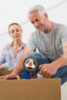 Happy couple sealing cardboard moving boxes