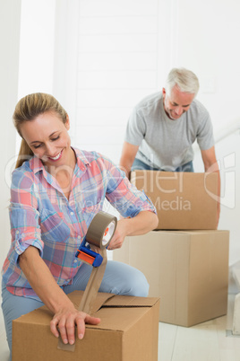 Happy couple sealing cardboard moving boxes