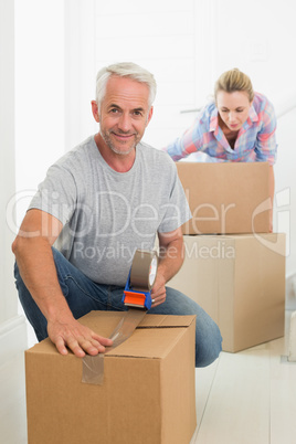 Happy couple sealing cardboard moving boxes