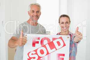 Happy couple standing and holding sold sign giving thumbs up
