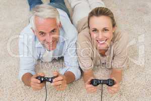 Smiling couple lying on rug playing video games