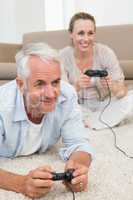 Smiling couple lying on rug playing video games