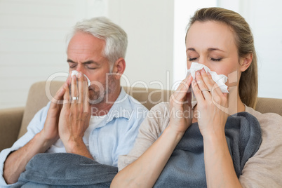 Sick couple blowing their noses sitting on the couch