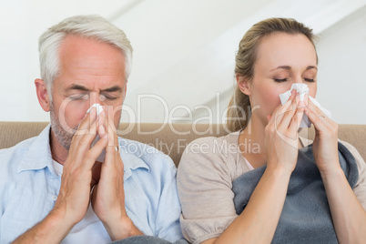 Sick couple blowing their noses sitting on the couch