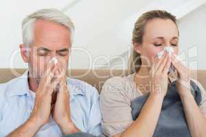 Sick couple blowing their noses sitting on the couch