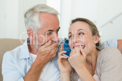 Happy couple listening to phone call together on the couch