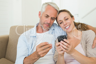 Happy couple sitting on couch texting on their phones Happy couple sitting on couch texting on their phones