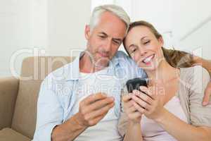 Happy couple sitting on couch texting on their phones